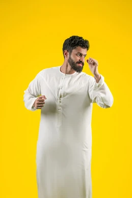 انشطة رياضية بدنية، ممارسة رياضة الدفاع عن النفس، التدرب على إتقان فنون الملاكمة، زيادة قدرة العضلات على التحمل، بورتريه لشاب عربي خليجي اماراتي يرتدي الكندورة يقفز ويرفع قبضات يديه بإيماءات القوة، خلفية صفراء