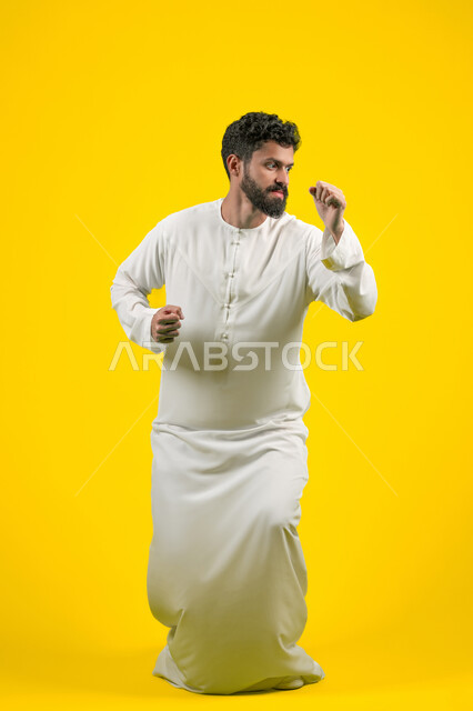 نشاط رياضي بدني، ممارسة رياضة الدفاع عن النفس، التدرب على إتقان فنون الملاكمة، زيادة قدرة العضلات على التحمل، بورتريه لشاب عربي خليجي اماراتي يرتدي الكندورة يقفز ويرفع قبضات يديه بإيماءات القوة، الجسم بالطول الكامل، خلفية صفراء