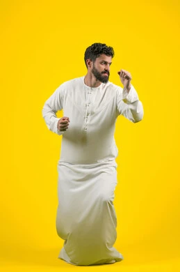 نشاط رياضي بدني، ممارسة رياضة الدفاع عن النفس، التدرب على إتقان فنون الملاكمة، زيادة قدرة العضلات على التحمل، بورتريه لشاب عربي خليجي اماراتي يرتدي الكندورة يقفز ويرفع قبضات يديه بإيماءات القوة، الجسم بالطول الكامل، خلفية صفراء