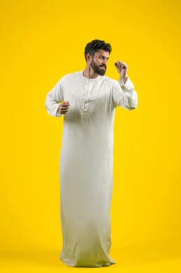 ممارسة رياضة الدفاع عن النفس، التدرب على إتقان فنون الملاكمة، زيادة قدرة العضلات على التحمل، بورتريه لشاب عربي خليجي اماراتي يرتدي الكندورة يقفز ويرفع قبضات يديه بإيماءات القوة، الجسم بالطول الكامل، خلفية صفراء