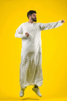 التدرب على إتقان فنون الملاكمة، زيادة قدرة العضلات على التحمل، بورتريه لشاب عربي خليجي اماراتي يرتدي الكندورة يقفز عاليا ويرفع قبضات يديه بإيماءات القوة، ممارسة رياضة الدفاع عن النفس، الجسم بالطول الكامل، خلفية صفراء