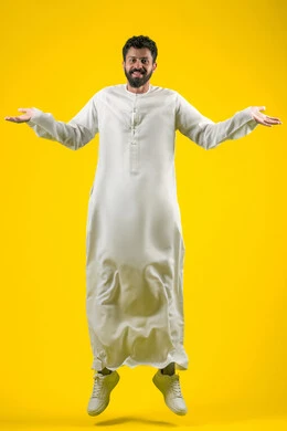 السخرية من موضوع مبهم، الاستغراب والاستفسار عن أمر ما، , بورتريه لشاب عربي خليجي إماراتي يرتدي الكندورة يقفز عاليا ينظر إلى الكاميرا ويرفع يديه نحو الأعلى بإيماءات عدم المعرفة, التردد وعدم الثقة، الشعور بالحيرة والغموض، الجسم بالطول الكامل، خلفية صفراء
