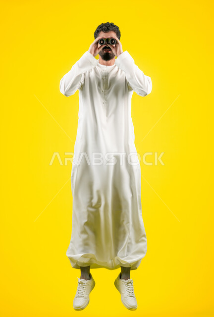 Searching for something and expanding the field of vision using binoculars, the concept of exploration and adventure, future visions of young people, portrait of a young Emirati Gulf Arab man wearing a kandura jumping high and looking through binoculars, full body length, yellow background