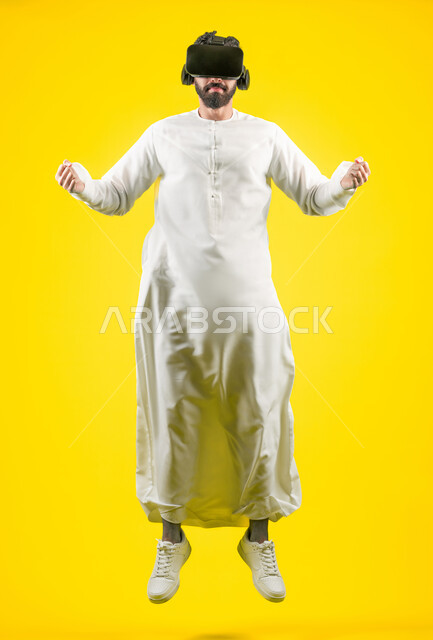 Enjoy watching movies and simulating the imaginary world, portrait of a young Emirati Gulf Arab man wearing a kandura and 3D VR glasses, interacting and merging with virtual reality games, jumping high and raising his fist to try to grab something, full body, yellow background