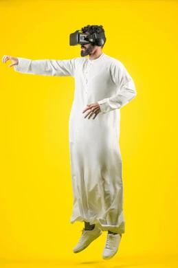 Jumping high and raising hands to try to catch something, enjoying watching movies and simulating the imaginary world, portrait of an Arab Gulf Emirati young man wearing a kandura and 3D VR glasses, interacting and merging with virtual reality games, full-length body, yellow background