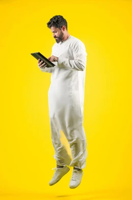 Using a tablet to complete work tasks, browsing social media applications, using modern and advanced technology, portrait of an Emirati Gulf Arab man wearing a kandura using a tablet with focus gestures, full body length, yellow background Using a tablet to complete work tasks, browsing social media applications, using modern and advanced technology, portrait of an Emirati Gulf Arab man wearing a kandura using a tablet with focus gestures, full body length, yellow background