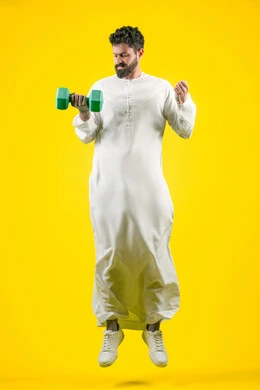 حرق الدهون والسعرات الحرارية, تعابير الثقة بالنفس، نشاط بدني للمحافظه على الصحة واللياقه الجسديه, ممارسة تمارين رفع الأثقال (دمبلز), بورتريه لرجل عربي خليجي اماراتي يرتدي الكندورة يحمل الاوزان الحديديه، الجسم بالطول الكامل، خلفية صفراء