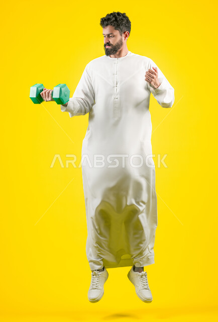 نشاط بدني للمحافظه على الصحة واللياقه الجسديه, حرق الدهون والسعرات الحرارية, تعابير الثقة بالنفس، ممارسة تمارين رفع الأثقال (دمبلز), بورتريه لرجل عربي خليجي اماراتي يرتدي الكندورة يحمل الاوزان الحديديه، الجسم بالطول الكامل، خلفية صفراء
