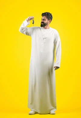استلام وتسليم المفاتيح، الحصول على رخصة القيادة، الحماس لامتلاك سيارة جديدة، خدمه صف السيارات بالمواقف الخاصه, بورتريه لشاب عربي خليجي اماراتي يرتدي الزي الكندورة يمسك بيده مفتاح التحكم عن بعد, الجسم بالطول الكامل، خلفية صفراء