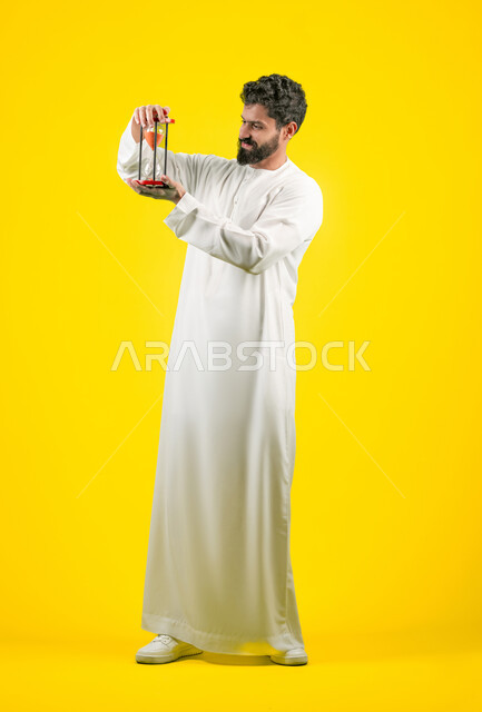 Sand time monitoring, realizing the value of precious moments, concept of business management and schedule organization, portrait of a young Emirati Gulf Arab man wearing a kandura holding a glass sand hourglass (bankam) with gestures of joy and happiness, full body, yellow background