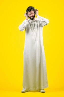الاستماع إلى الموسيقى, مواهب غنائية فنية، بورتريه لرجل عربي خليجي اماراتي يرتدي الكندورة يضع الهيدفون، إيماءات السعادة و الاندماج مع الأغنية، تسجيل مقطع صوتي غنائي، صورة الجسم بالكامل، خلفيه صفراء