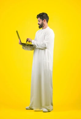 Using modern and advanced technology, using a laptop to complete remote work tasks, side portrait of an Emirati Gulf Arab man wearing a kandura using a computer with focus gestures, full body length, yellow background