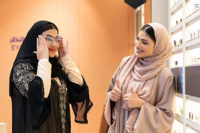 التأثير الإيجابي للتسوق على المرأة، اختيار نظارة شمسيه مناسبة ،متعة الشراء من احدي المولات الاماراتية، مفهوم الموضة والاناقة والاهتمام بالمظهر الخارجي، صديقتان عربيتان خليجيتان سعوديتان ترتديان العباءة يقومان باختيار النظاره الملائمه لملامح الوجه ، امرأة اماراتية تقوم بتجربة النظارات قبل الشراء