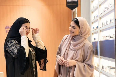 متعة الشراء من احدي المولات الاماراتية، مفهوم الموضة والاناقة والاهتمام بالمظهر الخارجي، احدث صيحات الموضة، صديقتان عربيتان خليجيتان سعوديتان ترتديان العباءة يقومان باختيار النظاره الملائمه لملامح الوجه ، امرأة اماراتية تقوم بتجربة النظارات قبل الشراء، التأثير الإيجابي للتسوق على المرأة، اختيار نظارة شمسيه مناسبة