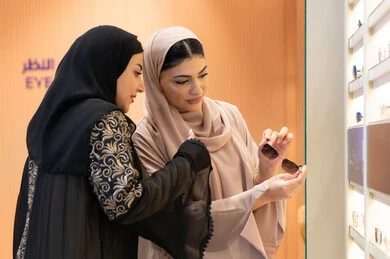 اختيار نظارة شمسيه مناسبة، احدث صيحات الموضة، صديقتان عربيتان خليجيتان سعوديتان ترتديان العباءة احداهما تقوم بقياس نظاره ، امرأة اماراتية تقوم بتجربة النظارات قبل الشراء، الاهتمام بالمظهر الخارجي،التأثير الإيجابي للتسوق على المرأة