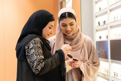 اختيار نظارة شمسيه مناسبة ، التأثير الإيجابي للتسوق على المرأة، متعة الشراء من احدي المولات الاماراتية، مفهوم الموضة والاناقة والاهتمام بالمظهر الخارجي، امرأة اماراتية تساعد صديقتها فى اختيار النظاره الملائمه لملامح الوجه ، صديقتان عربيتان خليجيتان سعوديتان ترتديان العباءة احداهما تقوم بقياس النظارة