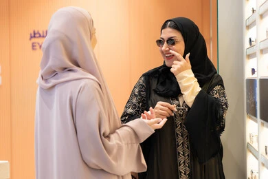 اختيار نظارة شمسيه مناسبة، احدث صيحات الموضة، صديقتان عربيتان خليجيتان سعوديتان ترتديان العباءة احداهما تقوم بقياس نظاره ورؤيتها على المرآة، امرأة اماراتية تقوم بتجربة النظارات قبل الشراء، الاهتمام بالمظهر الخارجي،التأثير الإيجابي للتسوق على المرأة