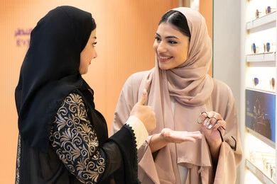 امرأة اماراتية تساعد صديقتها فى اختيار النظاره الملائمه لملامح الوجه ، صديقتان عربيتان خليجيتان سعوديتان ترتديان العباءة احداهما تقوم بقياس النظارة ،الاناقة والاهتمام بالمظهر الخارجي،  اختيار نظارة طبية مناسبة ، مفهوم ضعف البصر ، التأثير الإيجابي للتسوق على المرأة، متعة الشراء من احدي المولات الاماراتية