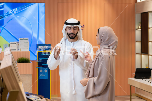 انواع وماركات عالميه ، الاناقة والاهتمام بالمظهر الخارجي، اقتناء الاكسسورات من المولات ، سيدة امارتية تساعد زوجها فى التسوق ، مواكبة آخر صيحات الموضة والجمال، مفهوم ضعف النظر، زوجان عربيان خليجيان اماراتيان يقومان باختيار نظارة طبية ملائمة لملامح الوجه