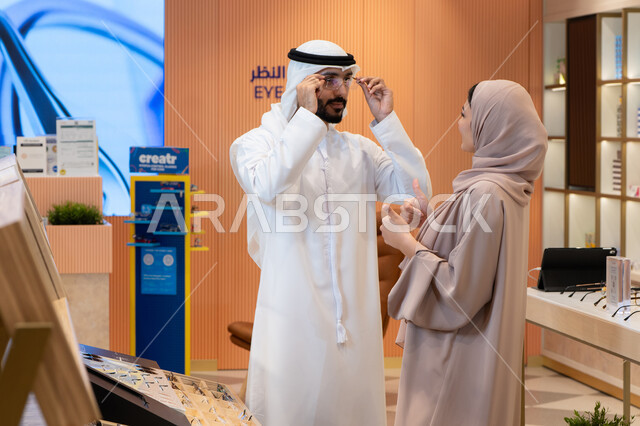 اقتناء الاكسسورات من المولات ، الاناقة والاهتمام بالمظهر الخارجي، سيدة امارتية تساعد زوجها فى التسوق ، مواكبة آخر صيحات الموضة والجمال، انواع وماركات عالميه ، مفهوم ضعف النظر، زوجان عربيان خليجيان اماراتيان يقومان باختيار نظارة طبية ملائمة لملامح الوجه