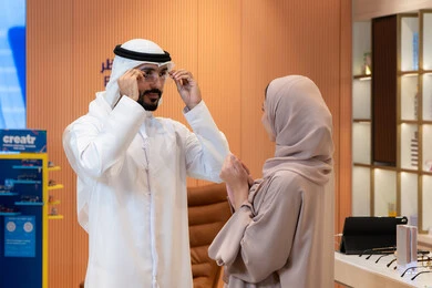 An Emirati woman helps her husband in shopping, keeping up with the latest fashion and beauty trends, international brands and types, the concept of weak eyesight, elegance and interest in appearance, buying accessories from malls, an Arab Gulf Emirati couple choosing eyeglasses that suit their facial features