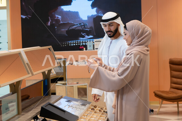 انواع وماركات عالميه ، مفهوم ضعف النظر، الاناقة والاهتمام بالمظهر الخارجي، اقتناء الاكسسورات من المولات ، مواكبة آخر صيحات الموضة والجمال،  زوجان عربيان خليجيان اماراتيان يقومان باختيار نظارة طبية ملائمة لملامح الوجه، المتعة بالتسوق في مولات الإمارات
