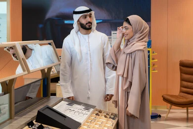 مفهوم ضعف النظر،الاناقة والاهتمام بالمظهر الخارجي، مواكبة آخر صيحات الموضة والجمال، اقتناء الاكسسورات من المولات ، انواع وماركات عالميه، المتعة بالتسوق في مولات الإمارات،زوجان عربيان خليجيان اماراتيان يقومان باختيار نظارة طبية ملائمة لملامح الوجه