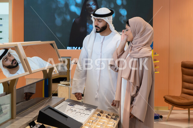 الاناقة والاهتمام بالمظهر الخارجي، مواكبة آخر صيحات الموضة والجمال، اقتناء الاكسسورات من المولات ،مفهوم ضعف النظر، انواع وماركات عالميه، المتعة بالتسوق في مولات الإمارات،زوجان عربيان خليجيان اماراتيان يقومان باختيار نظارة طبية ملائمة لملامح الوجه