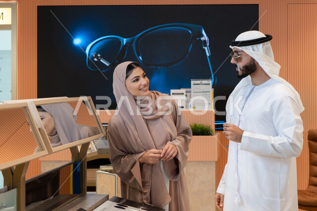 Benefit from offers and discounts, enjoy shopping in the malls of the Emirates, keep up with the latest fashion and beauty trends, elegance and attention to one's appearance, an Arab Gulf Emirati couple choosing sunglasses that suit their facial features, protecting their eyes from the sun's rays