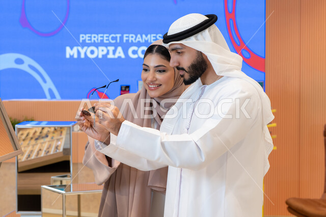 Protecting your eyes from the sun, being elegant and taking care of your appearance, enjoying shopping in the UAE malls, keeping up with the latest fashion and beauty trends, an Emirati Gulf Arab couple choosing sunglasses that suit their facial features.