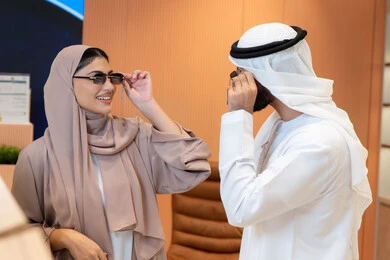 حماية العينين من أشعة الشمس، المتعة بالتسوق في مولات الإمارات، الاهتمام بالمظهر الخارجي، مواكبة آخر صيحات الموضة والجمال،زوجان عربيان خليجيان اماراتيان يقومان باختيار نظارة شمسية ملائمة لملامح الوجه