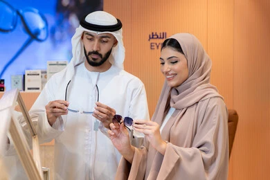 المتعة بالتسوق في مولات الإمارات، الاهتمام بالمظهر الخارجي،مواكبة آخر صيحات الموضة والجمال، حماية العينين من أشعة الشمس، زوجان عربيان خليجيان اماراتيان يقومان باختيار نظارة شمسية ملائمة لملامح الوجه