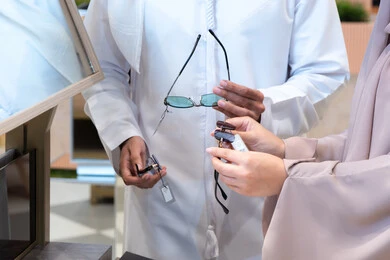 التسوق وشراء النظارات الشمسيه من المولات ،مفهوم الاناقه والاهتمام بالمظهر الخارجي، صورة مقربه لزوجان عربيان اماراتيان خليجيان يقومان باختيار النظارة الشمسيه المناسبة في محل نظارات