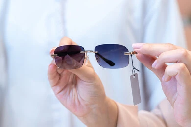 التسوق وشراء النظارات الشمسيه من المولات ، صورة مقربه ليد امراه عربيه اماراتيه خليجيه ترتدي العباءه تقوم باختيار النظارة الشمسيه المناسبة في محل نظارات ، مفهوم الاناقه والاهتمام بالمظهر الخارجي