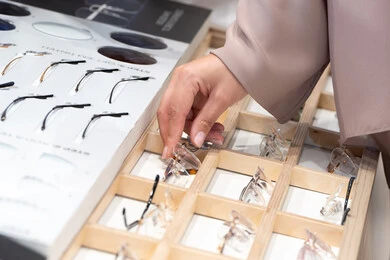 الاهتمام بالمظهر الخارجي، متعة التسويق والشراء ، الحيرة في اختيار نظارة مناسبة، الركن الخاص بالنظارات الطبية ، فحص النظارات الطبيه قبل الشراء،صورة مقربة ليد امراه عربية خليجية اماراتية ترتدي العباءه تقوم باختيار نظاره طبيه