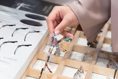 متعة التسويق والشراء ، الحيرة في اختيار نظارة مناسبة، الركن الخاص بالنظارات الطبية ، فحص النظارات الطبيه قبل الشراء،صورة مقربة ليد امراه عربية خليجية اماراتية ترتدي العباءه تقوم باختيار نظاره طبيه