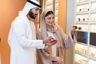 Attention to appearance and elegance, discounts and offers, an Emirati Arab couple choosing the right sunglasses in an Emirati store, the section for luxury sunglasses, shopping and purchasing from one of the Emirati malls.
