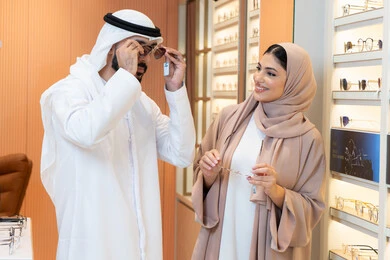 الركن الخاص بالنظارات الشمسيه الفخمه، التسوق والشراء من احدي المولات الاماراتيه، الاهتمام بالمظهر الخارجي والاناقه ، تخفيضات وخصومات وعروض، زوجان عربيان خليجيان اماراتيان يقومان بقياس النظارة الشمسيه المناسبة في محل اماراتي