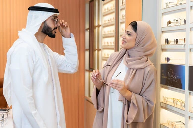 التسوق والشراء من احدي المولات الاماراتيه، الاهتمام بالمظهر الخارجي والاناقه ، تخفيضات وخصومات وعروض، الركن الخاص بالنظارات الشمسيه الفخمه، زوجان عربيان خليجيان اماراتيان يقومان بقياس النظارة الشمسيه المناسبة في محل اماراتي
