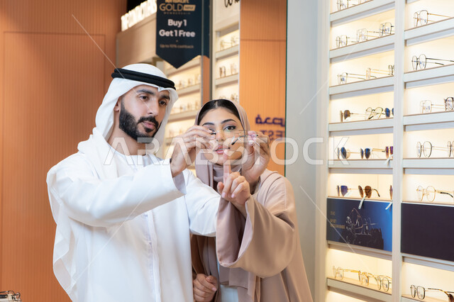 التسوق والشراء من المولات، الاهتمام بالمظهر الخارجي والاناقه ، سيدة اماراتية تساعد الزبائن فى الاختيار ،الركن الخاص بالنظارات الشمسيه الفخمه، رجل عربي خليجي اماراتي يرتدي الكندورة والغترة يقوم بقياس النظارة الشمسيه المناسبة في محل اماراتي، تخفيضات وخصومات وعروض