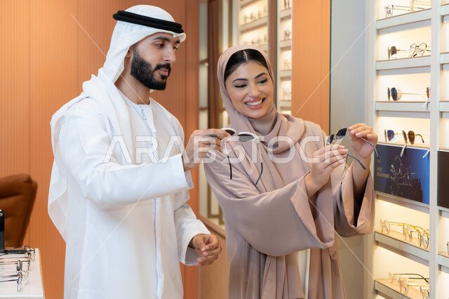 التسوق والشراء من المولات، سيدة اماراتية تساعد الزبائن ، الركن الخاص بالنظارات الشمسيه الفخمه، الاهتمام بالمظهر الخارجي والاناقه ،رجل عربي خليجي اماراتي يرتدي الكندورة والغترة يقوم بقياس النظارة الشمسيه المناسبة في محل اماراتي، تخفيضات وخصومات وعروض