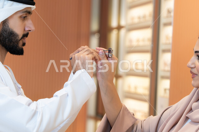 رجل عربي خليجي اماراتي يرتدي الكندورة والغترة يقوم بقياس النظارة الشمسيه المناسبة في محل اماراتي، تخفيضات وخصومات وعروض ،الاهتمام بالمظهر الخارجي والاناقه ، الركن الخاص بالنظارات الشمسيه الفخمه، التسوق وشراء النظارات الشمسيه من المولات