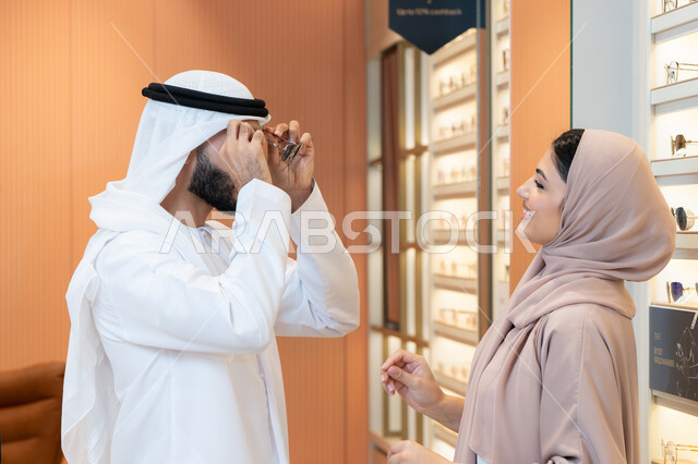 الاهتمام بالمظهر الخارجي والاناقه ، الركن الخاص بالنظارات الشمسيه الفخمه، رجل عربي خليجي اماراتي يرتدي الكندورة والغترة يقوم بقياس النظارة الشمسيه المناسبة في محل نظارات، تخفيضات وخصومات وعروض ، التسوق وشراء النظارات الشمسيه من المولات
