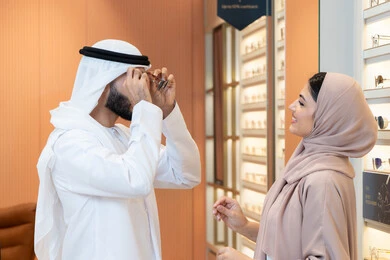 Attention to appearance and elegance, the section dedicated to luxury sunglasses, an Arab Gulf Emirati man wearing a kandura and ghutrah is trying on the suitable sunglasses in an eyewear shop, discounts and offers, shopping and buying sunglasses from malls.