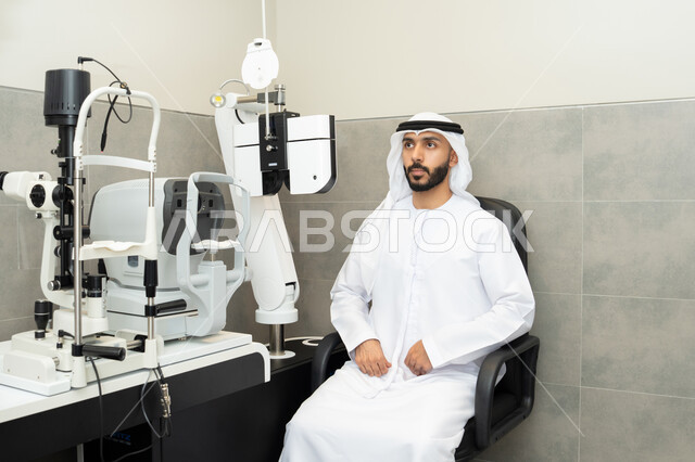 تقييم مدى الرؤية والكشف عن الامراض العينية،استخدام الأجهزة الحديثة المتطورة، تشخيص وتحديد المشاكل البصرية، مفهوم الخدمات والرعاية الصحية في المستشفيات والمراكز،رجل عربي خليجي اماراتي يرتدي الزي التقليدي امام جهاز فحص العين للتأكد من صحة البصر