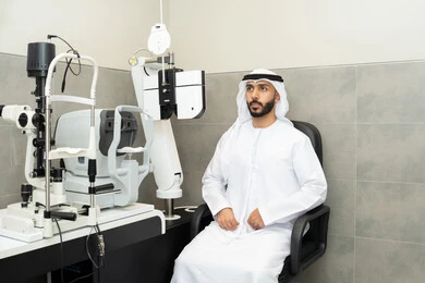 تقييم مدى الرؤية والكشف عن الامراض العينية،استخدام الأجهزة الحديثة المتطورة، تشخيص وتحديد المشاكل البصرية، مفهوم الخدمات والرعاية الصحية في المستشفيات والمراكز،رجل عربي خليجي اماراتي يرتدي الزي التقليدي امام جهاز فحص العين للتأكد من صحة البصر