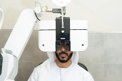 The use of advanced modern devices, diagnosing and identifying visual problems, assessing the range of vision and detecting eye diseases, the concept of services and healthcare in hospitals and centers, an Arab Gulf Emirati man wearing traditional attire in front of an eye examination device to ensure the health of his vision.