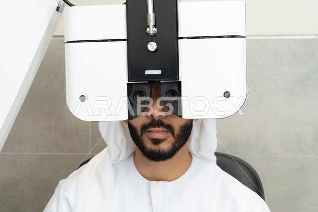 Diagnosis and identification of visual problems, use of advanced modern devices, the concept of services and healthcare in hospitals and medical centers, ensuring the accuracy of vision, an Arab Gulf Emirati man examining his eyes with an ophthalmoscope, assessing the extent of vision and detecting eye diseases.
