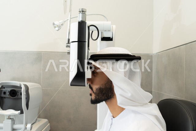 استخدام الأجهزة الحديثة المتطورة، مفهوم الخدمات والرعاية الصحية في المشافي والمراكز الطبية، التأكد من صحة البصر ، رجل عربي خليجي اماراتي يقوم بفحص عينيه بجهاز المنظار العيني، تشخيص وتحديد المشاكل البصرية، تقييم مدى الرؤية والكشف عن الامراض العينية