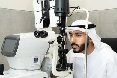 The concept of healthcare services and medical care in hospitals and medical centers, assessing the extent of vision and detecting eye diseases, using advanced modern devices, an Arab Gulf Emirati man examining his eyes with an ophthalmoscope, diagnosing and identifying visual problems, ensuring the health of vision.